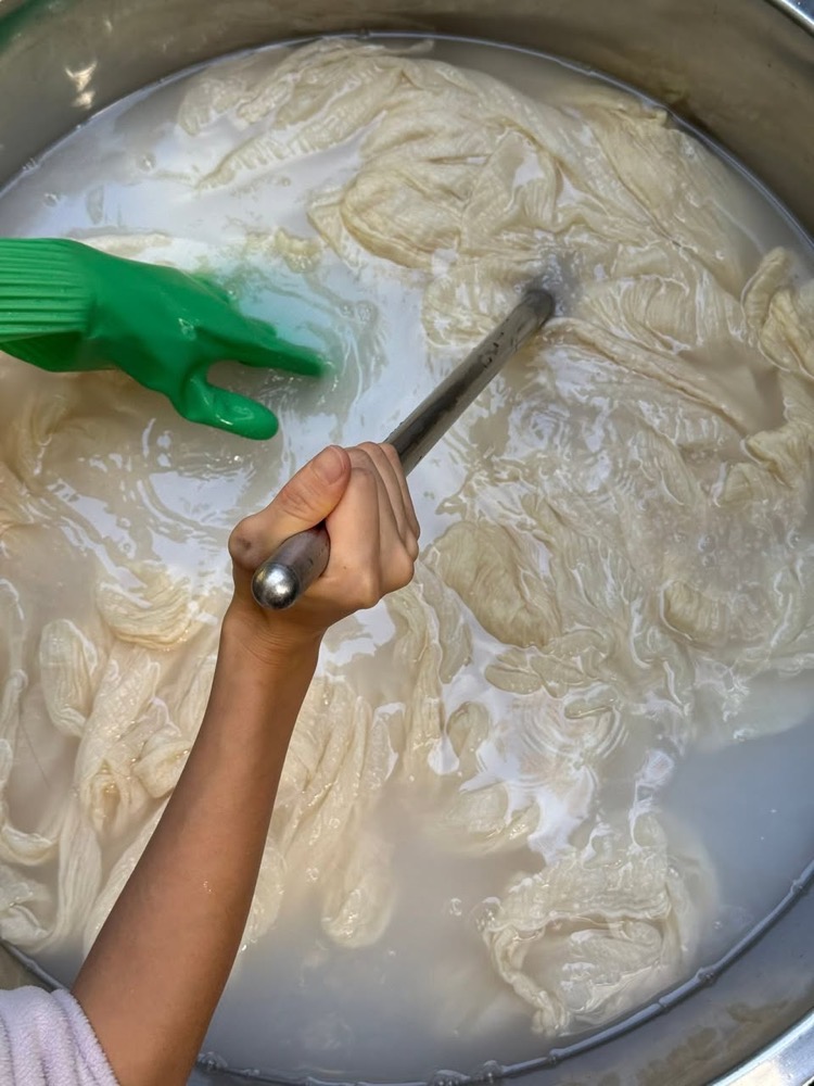 孩子戴著手套,用長棍在染缸裡攪動布料
