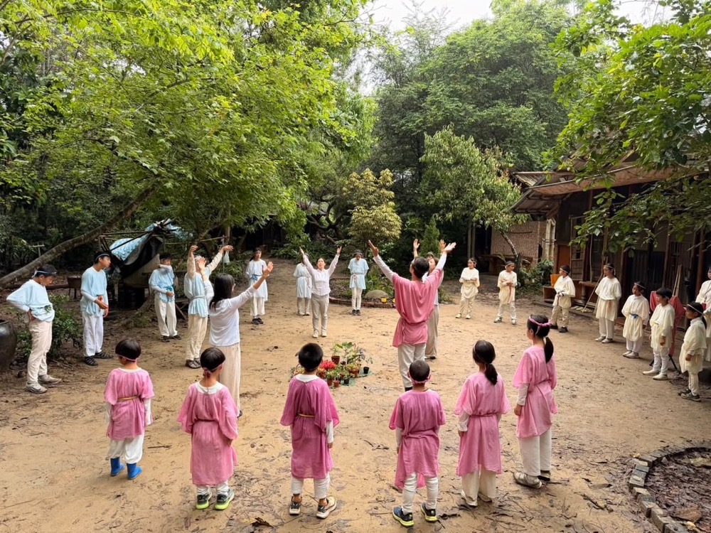 春之慶典中，孩子與老師在樹林間圍成圓圈，伸展手臂